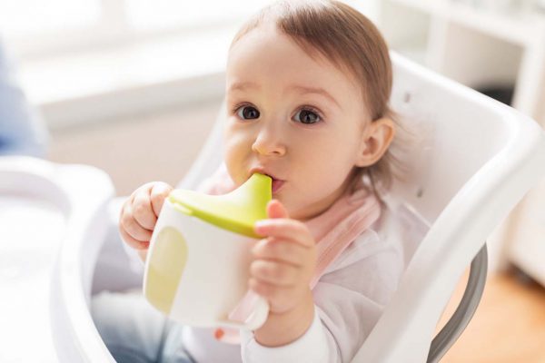 baby drinking from spout cup in highchair at home