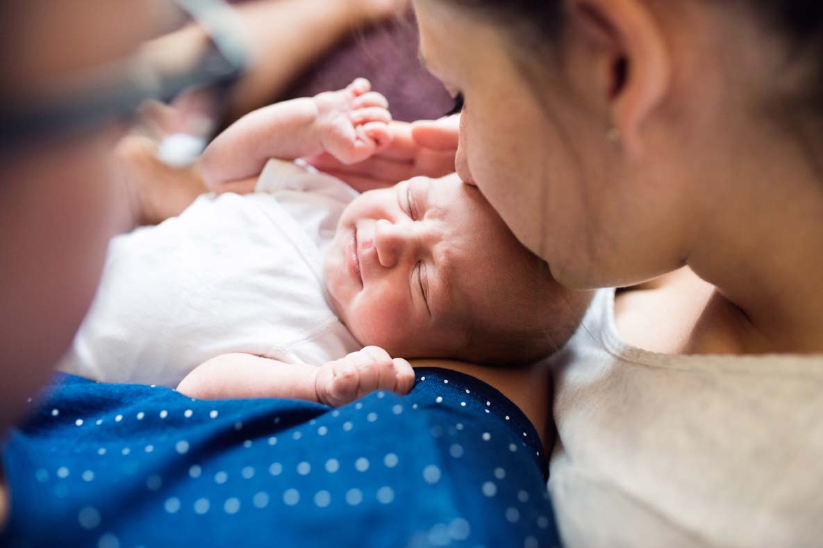Unrecognizable parents holding their newborn baby son, kissing h